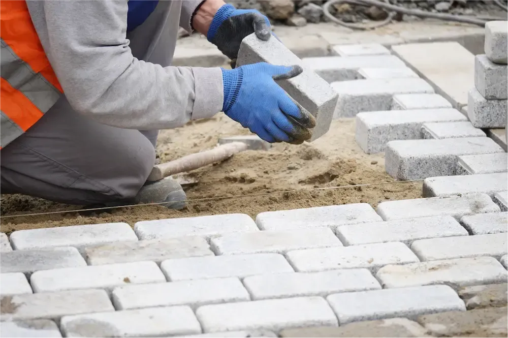 Worker laying white paving bricks on a sandy construction site