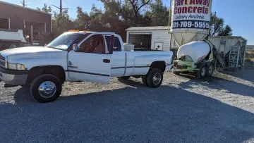 White pickup truck on a gravel lot beside a damaged boat and sign for a concrete business.