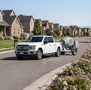 White pickup truck towing a gray tank trailer on a suburban street lined with houses