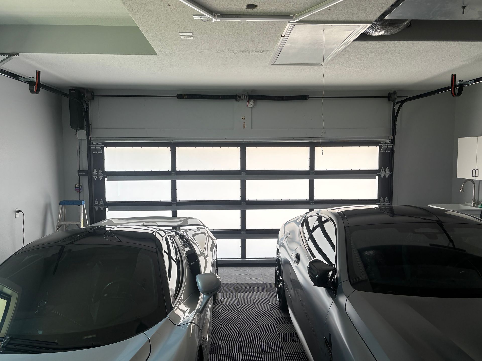 A garage with a partially open frosted glass door, two silver cars parked inside.