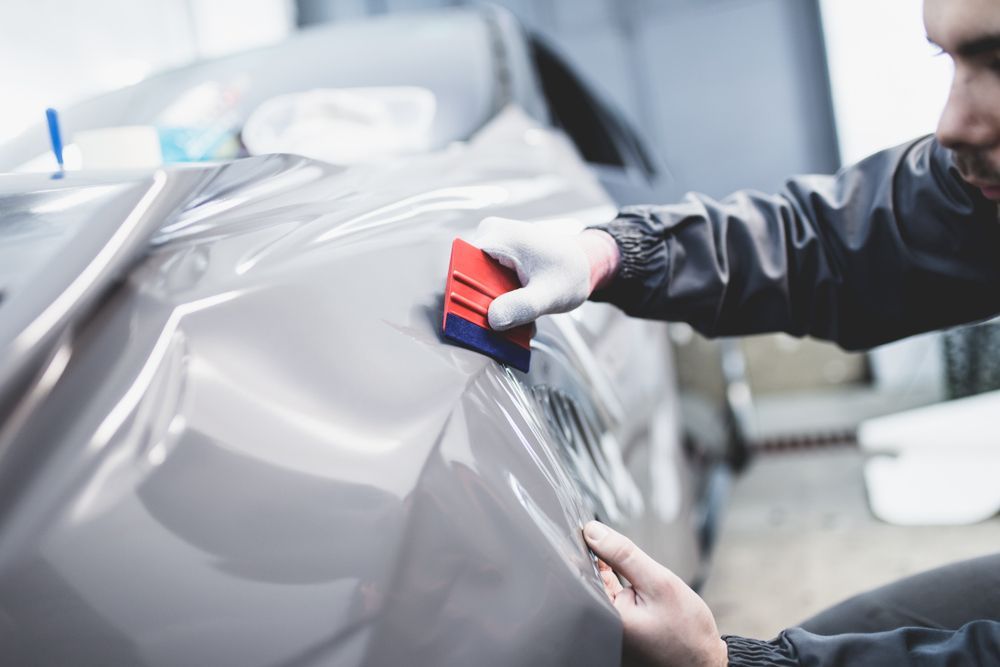 Hands Smoothing a Gray Vinyl Wrap on a Car in a Workshop — FNQ Paintless Dent Repair in Edmonton, QLD