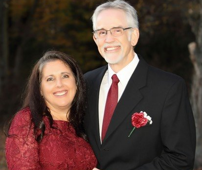 Couple smiles, posing outdoors. Woman in red dress, man in suit with red tie.