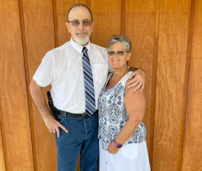 Man in uniform and woman in tank top pose together, standing in front of a wood wall.