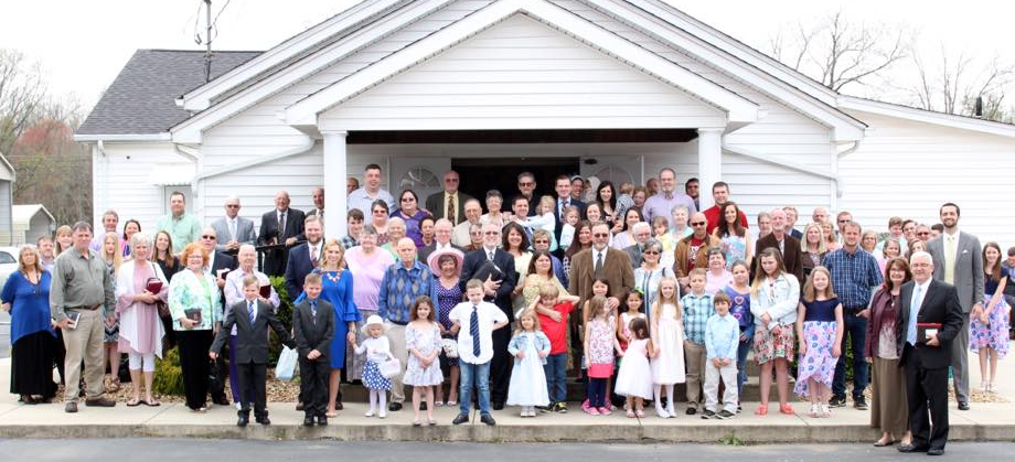 Group of people posing for a photo in front of a white church.