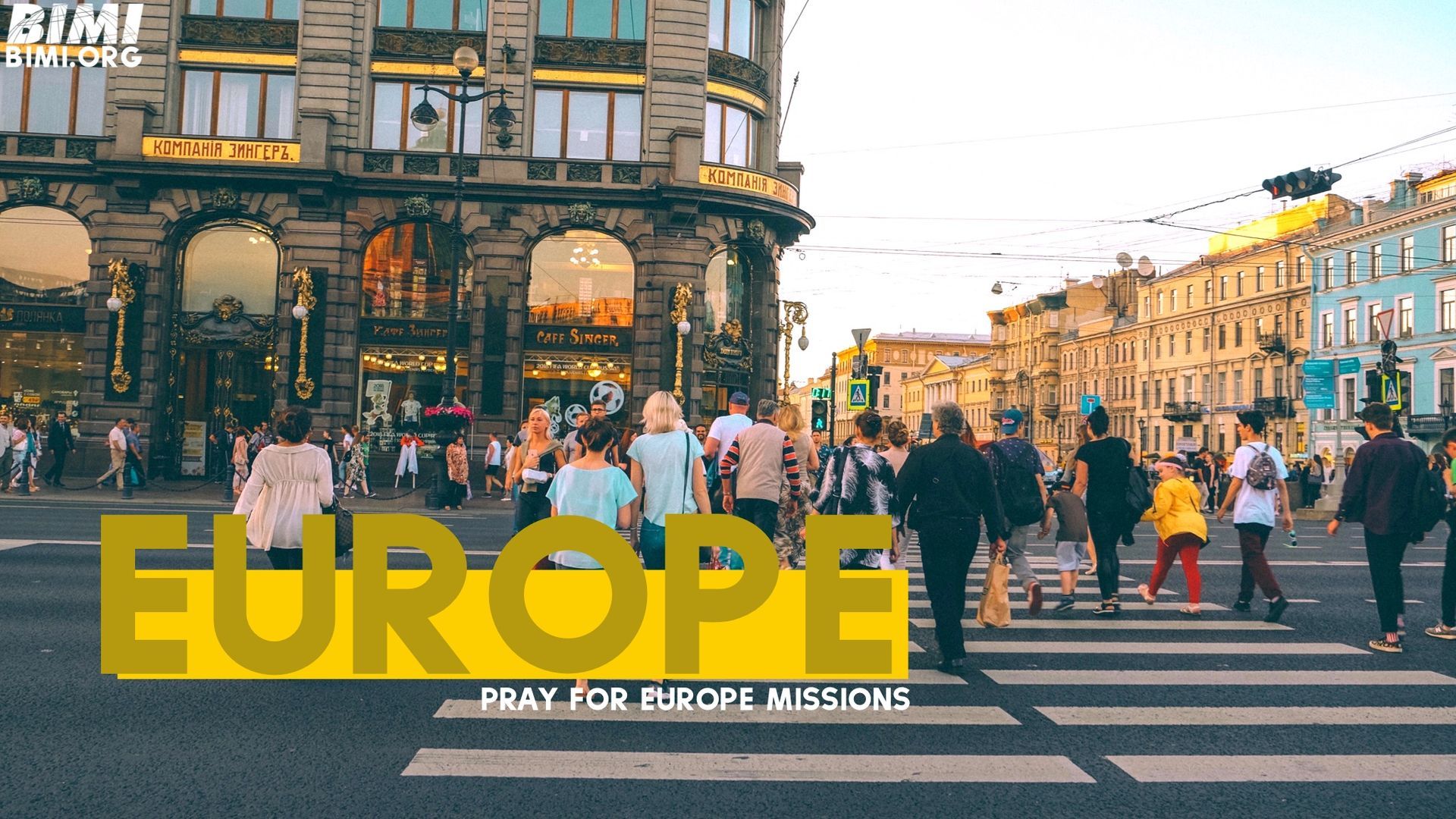 Crowd crossing a European street in front of ornate buildings. Text 