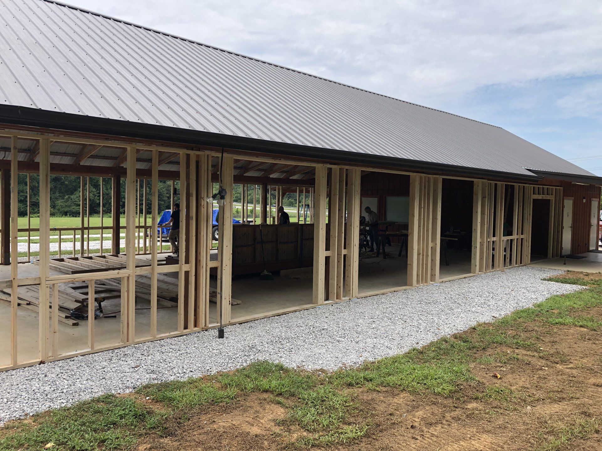 Construction of a building with exposed wooden framing and a metal roof. A gravel trench is visible along the side.