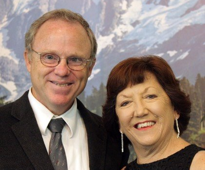 Man and woman smiling, posed closely together in front of a mountain scene backdrop.