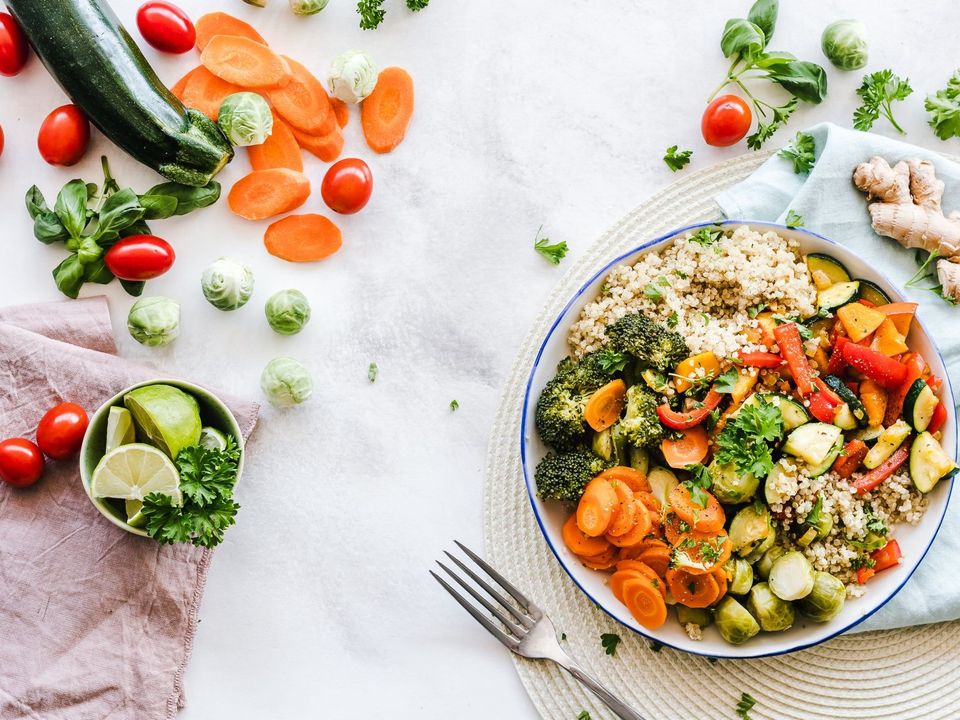 A plate of vegetables with rice and a fork on a table.