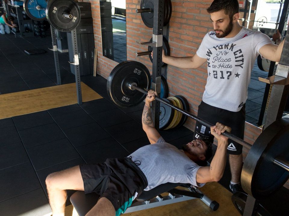 A man is lifting a barbell on a bench in a gym.