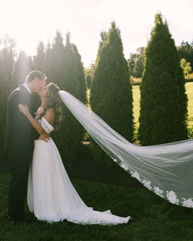 A bride and groom kissing in a field with trees in the background