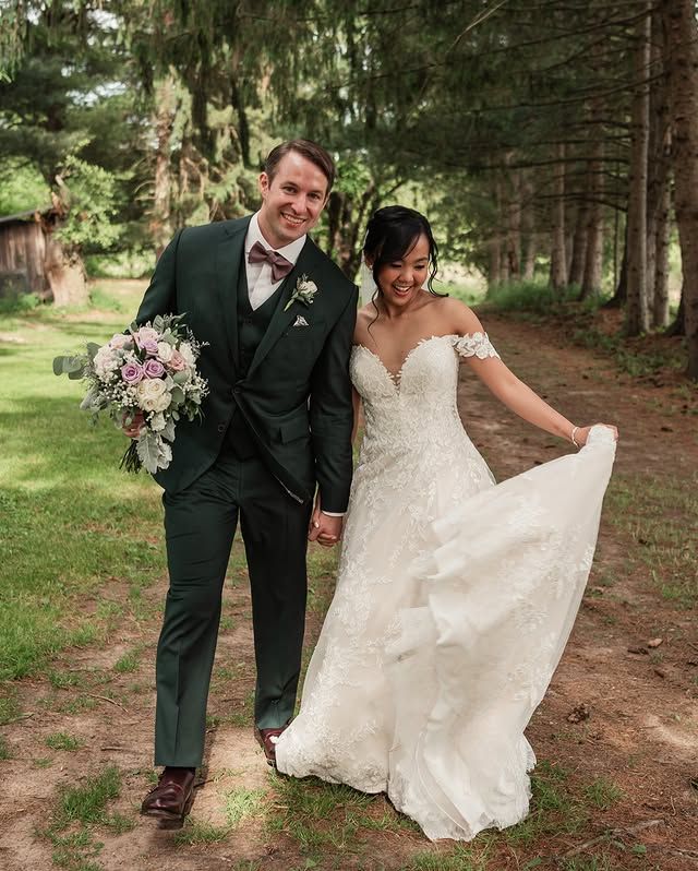 A bride and groom are walking in the woods holding hands.