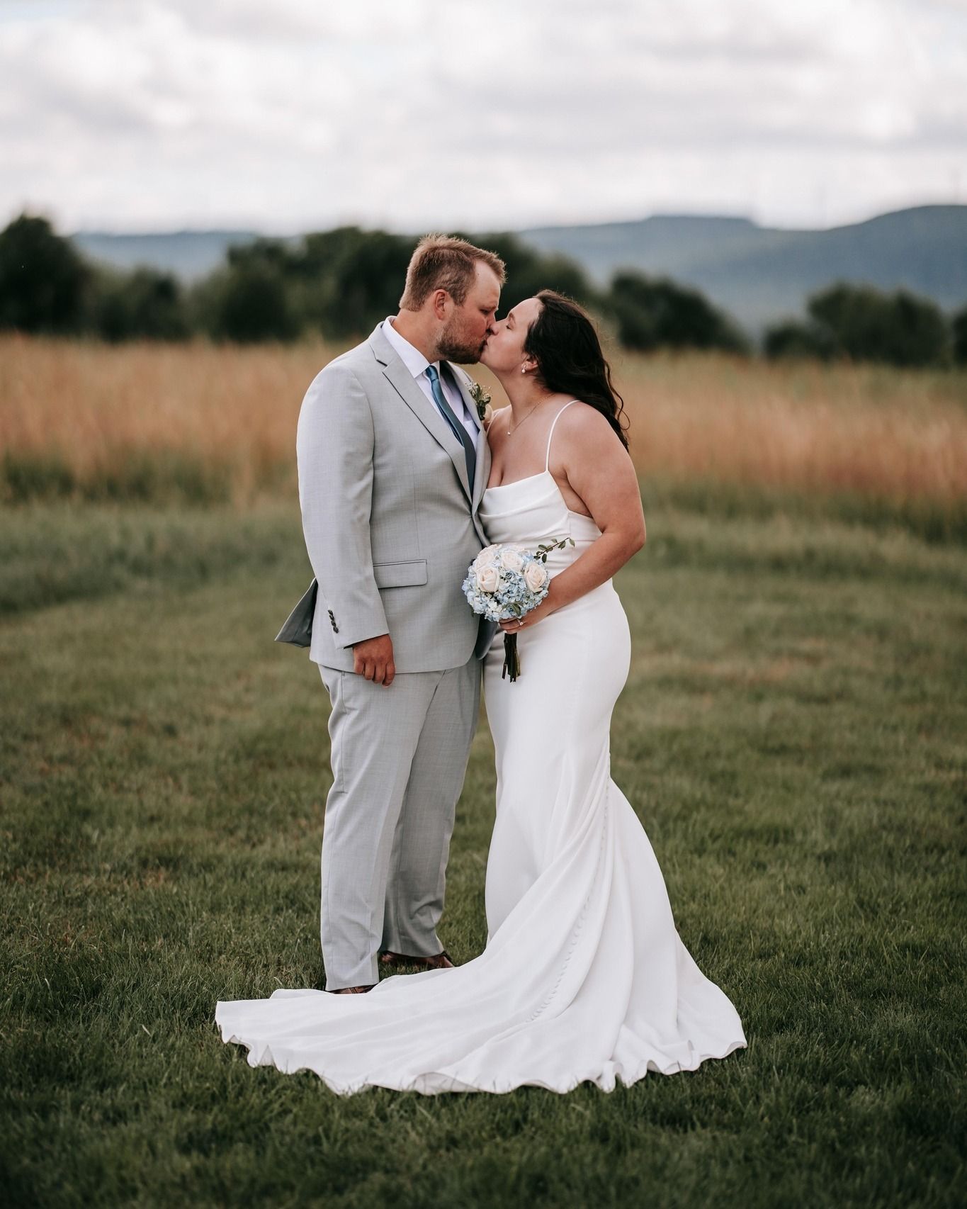 A bride and groom kissing in a field on their wedding day