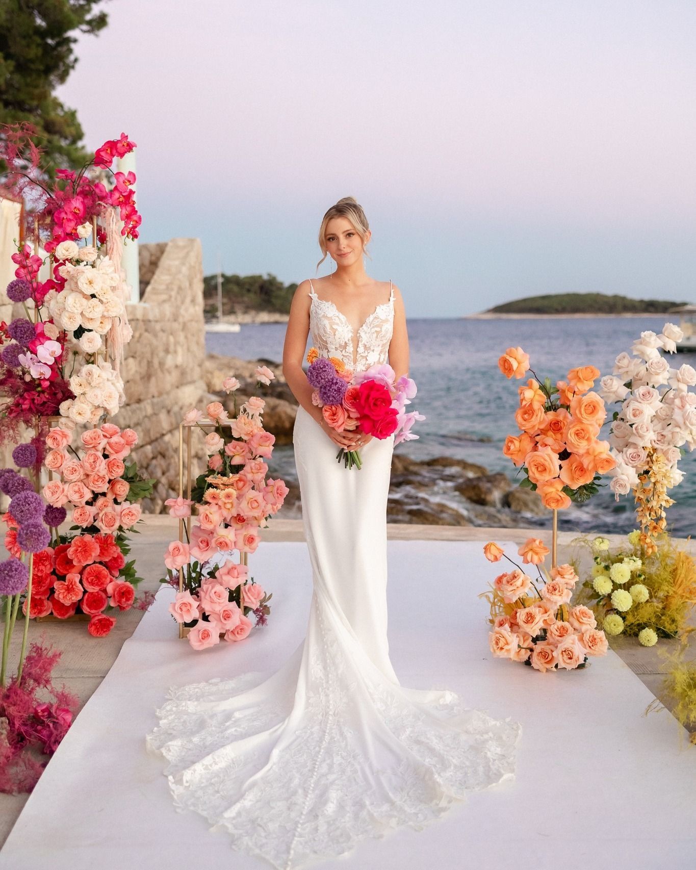 A bride in a white wedding dress is standing in front of a display of flowers.