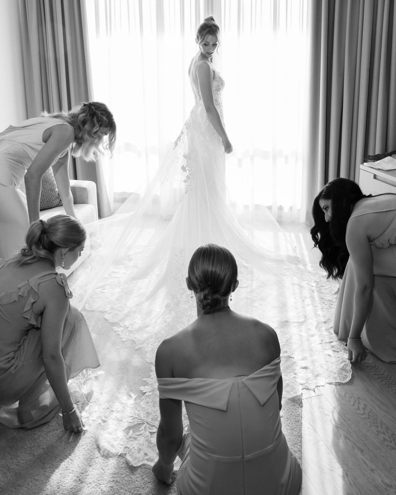 A black and white photo of a bride and her bridesmaids getting ready for her wedding.