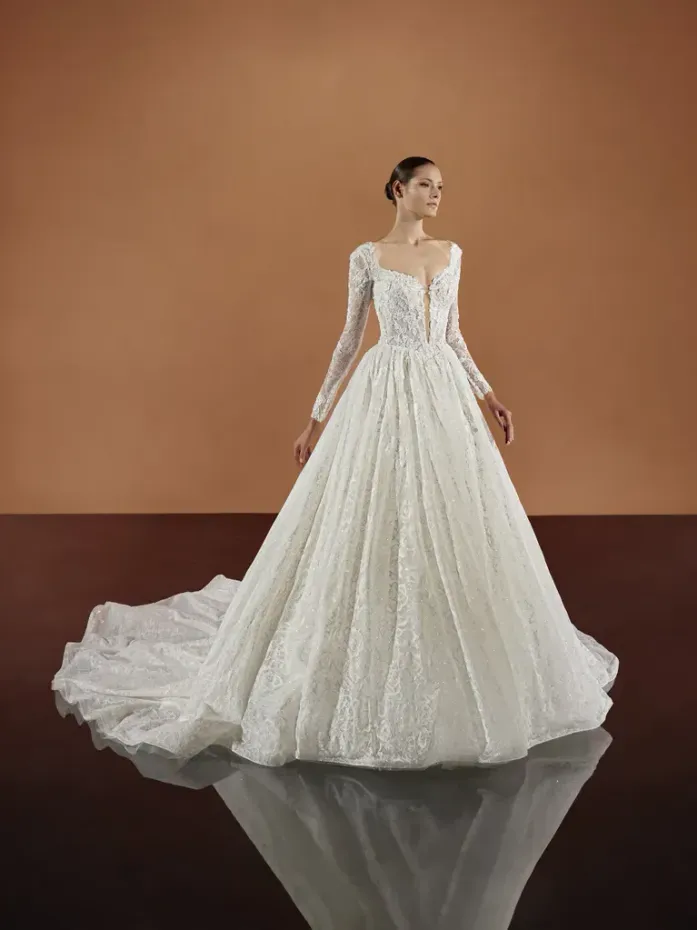 A woman is wearing a white wedding dress with long sleeves and a train.