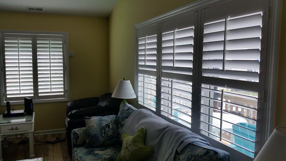 A living room with a couch , chair , lamp and shutters on the windows.