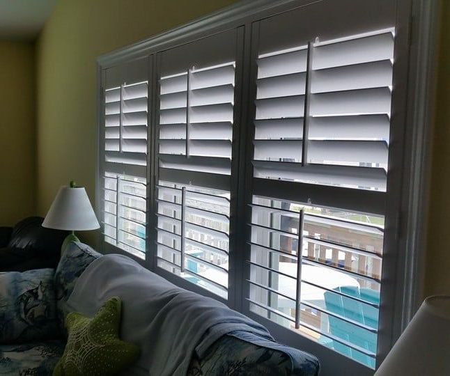 Living room with white window shutters and a sofa beside a lamp, daylight filtering through at Morehead City NC.
