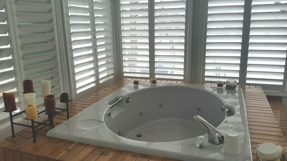 A jacuzzi tub in a bathroom with shutters and candles.