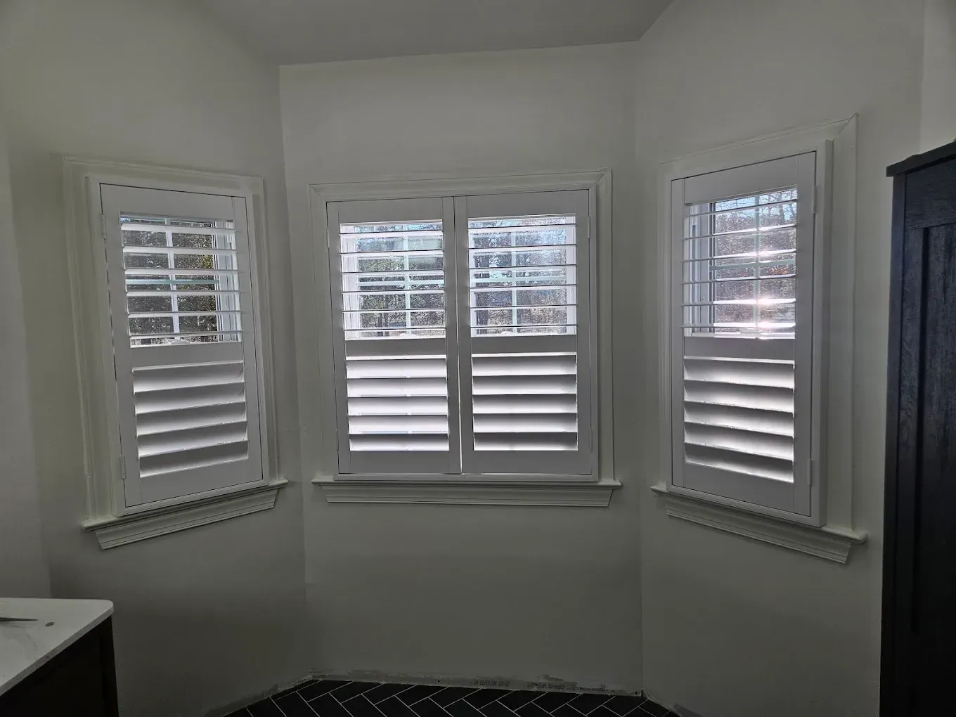 White room corner with three windows and white plantation shutters.