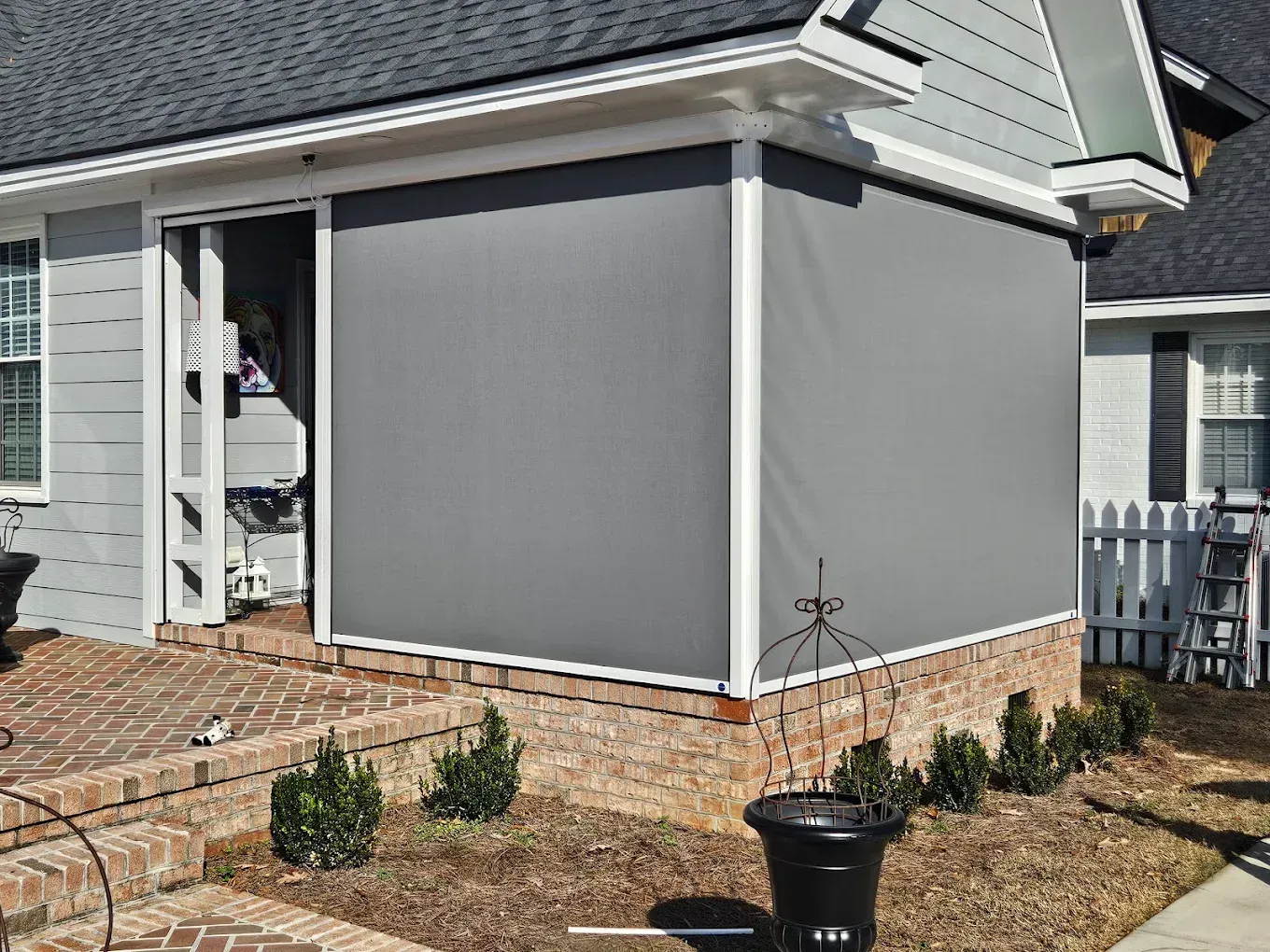 Gray-sided house addition with white trim and brick foundation, shown beside a front walkway and shrubs in Morehead City, NC.
