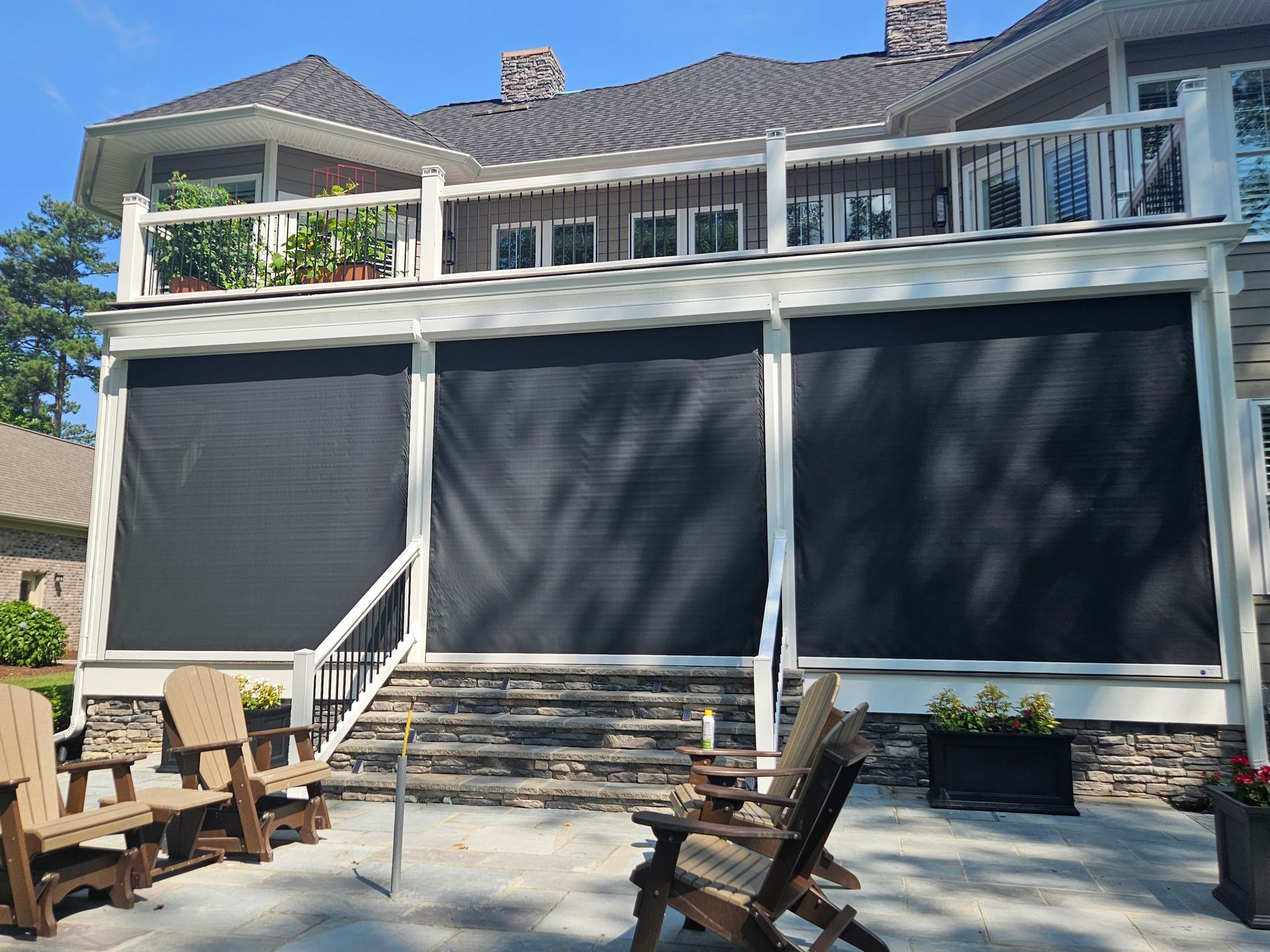 Patio with black sun shades, wood chairs, and a two-story home with a white railing in Washington, NC.