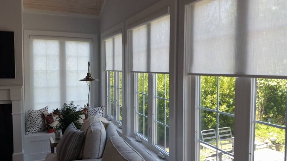 Sunroom with sheer roller shades; white trim, windows with a view of greenery in Washington, NC.