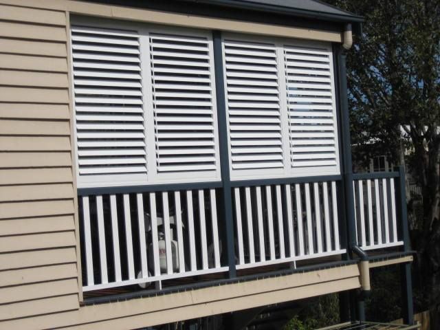 A balcony with white shutters and a black railing