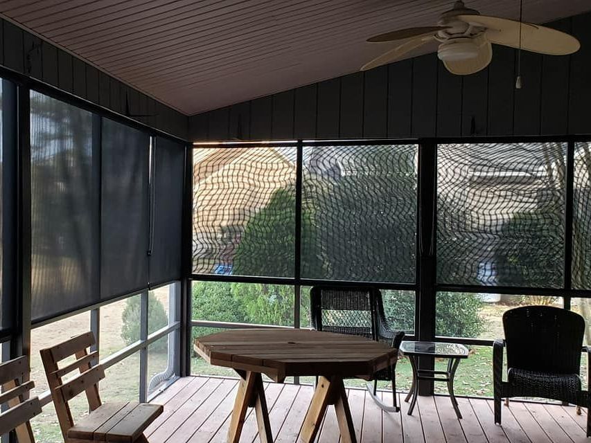 Screened porch with wooden furniture, overlooking a yard. Black screens and shades. Brown ceiling and floor in Washington, NC.