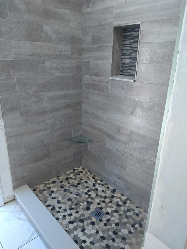 A walk in shower with a tiled wall and a mosaic floor.