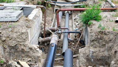 Pipes in an excavated trench, showing plumbing infrastructure. Brown and black pipes are exposed in dirt.