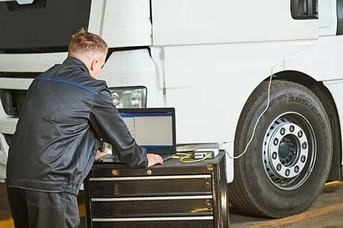 Mechanic diagnosing truck tire, connecting to computer with white truck and garage.