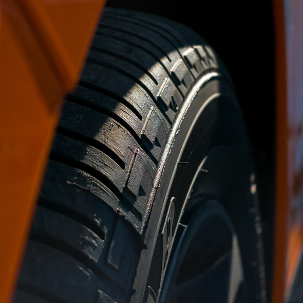 Close-up of an orange car tire, showing tread pattern and a partial view of the rim.