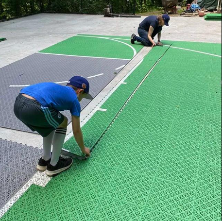 Workers carefully aligning and installing interlocking green sport court tiles with measuring tools to create a smooth playing surface during a court installation service in Chandler, AZ