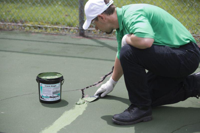 Worker applying sealant to repair cracks on a sport court surface using a brush during a court installation service in Chandler, AZ