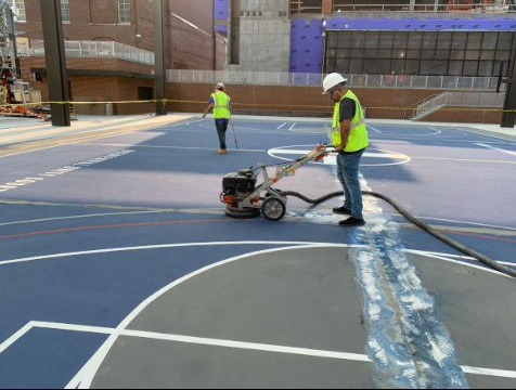 Worker using a floor grinder to remove old coating and prepare a sport court surface during a court installation service in Chandler, AZ