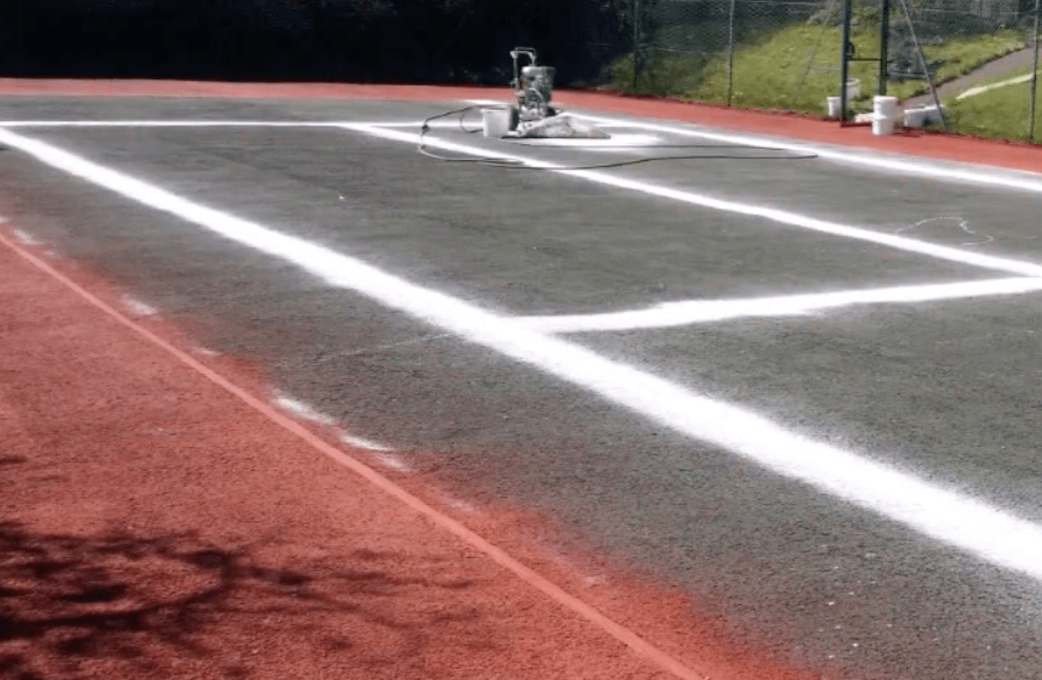 Worker preparing and cleaning a sport court surface before coating during a court installation service in Chandler, AZ