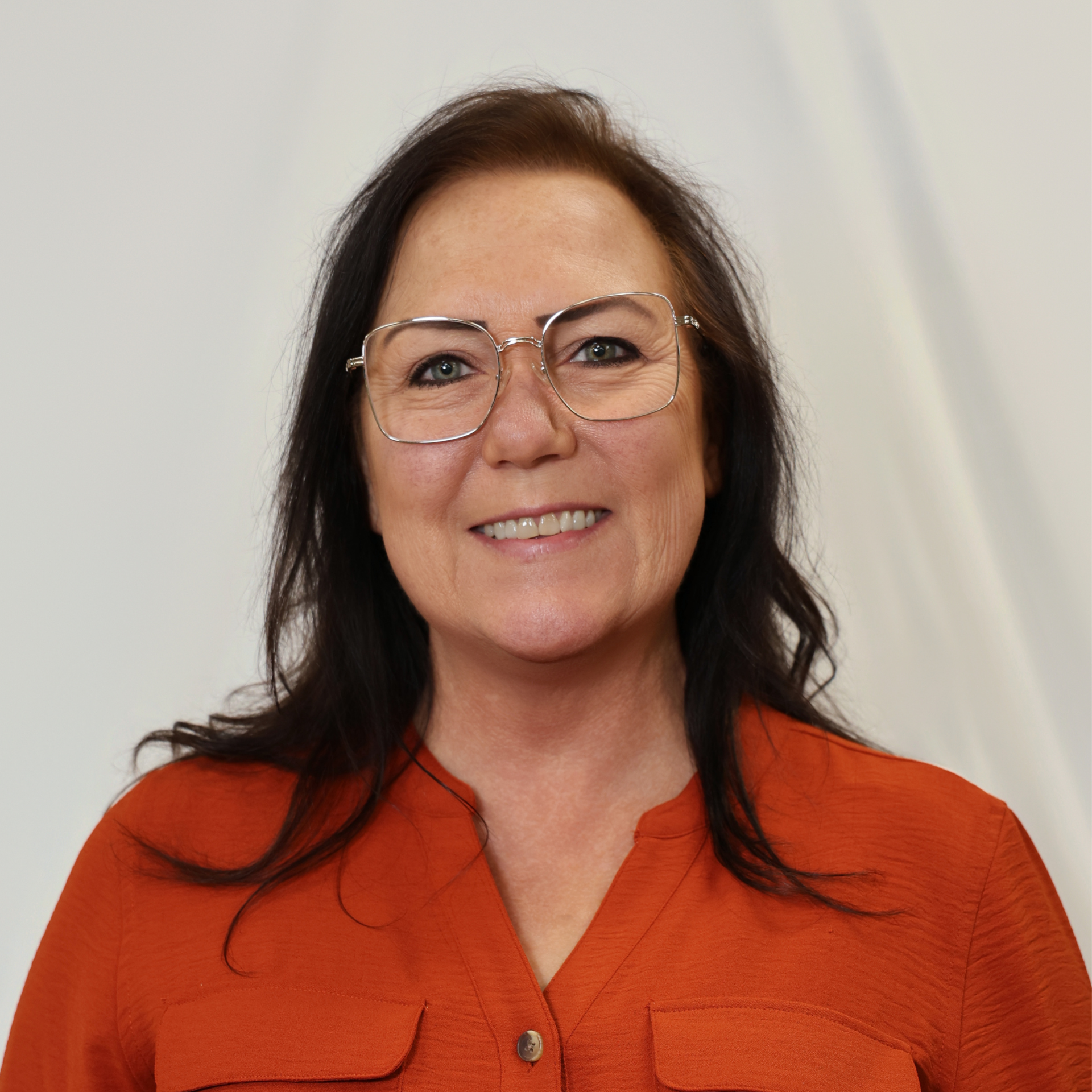 A woman wearing glasses and an orange sweater is smiling to the camera.