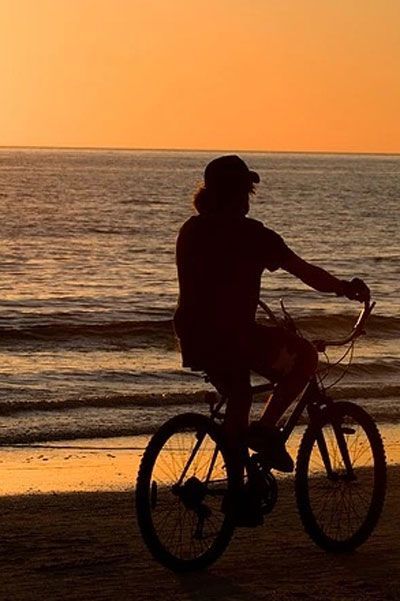 Two people riding bicycles on the beach at sunset