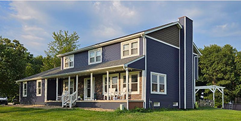 A large blue house with new siding is sitting on top of a lush green field