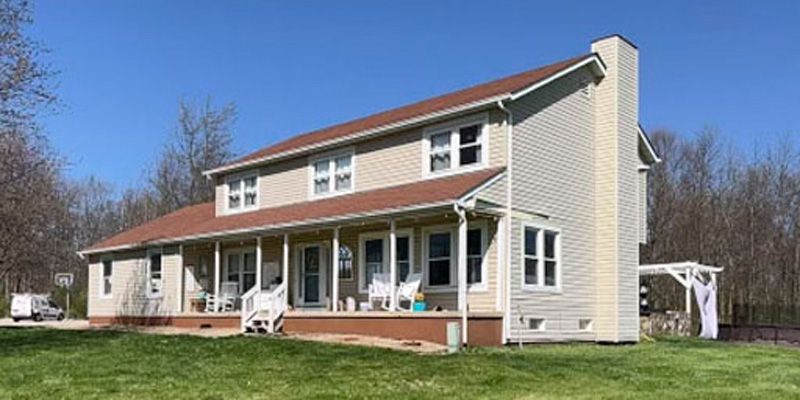 a large white house with outdated siding is sitting on top of a lush green field