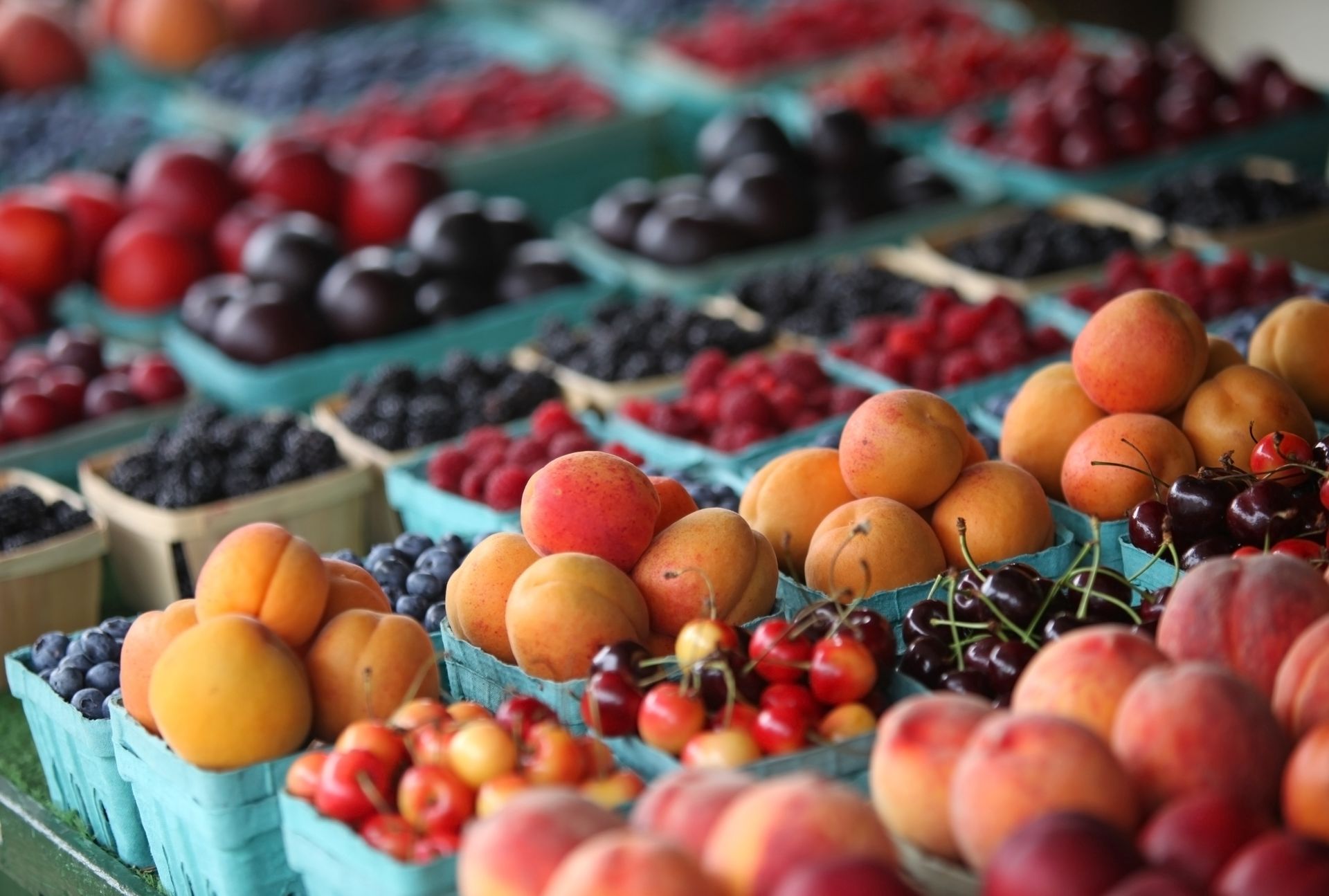 Assorted fresh fruit displayed in crates at an outdoor market, with oranges, peaches, and berries visible