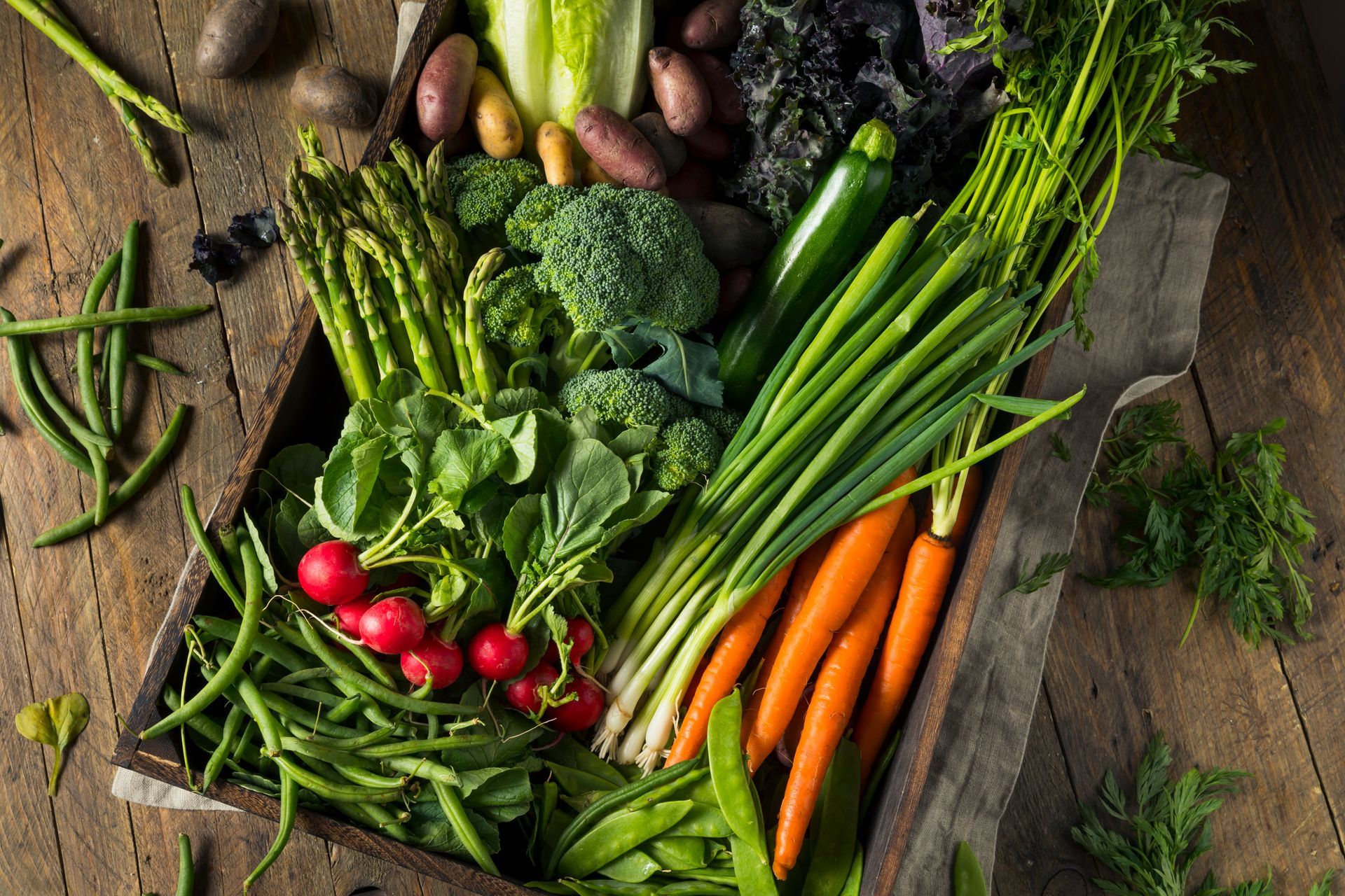Assorted fresh vegetables on a rustic table, including carrots, broccoli, radishes, green beans, and leafy greens