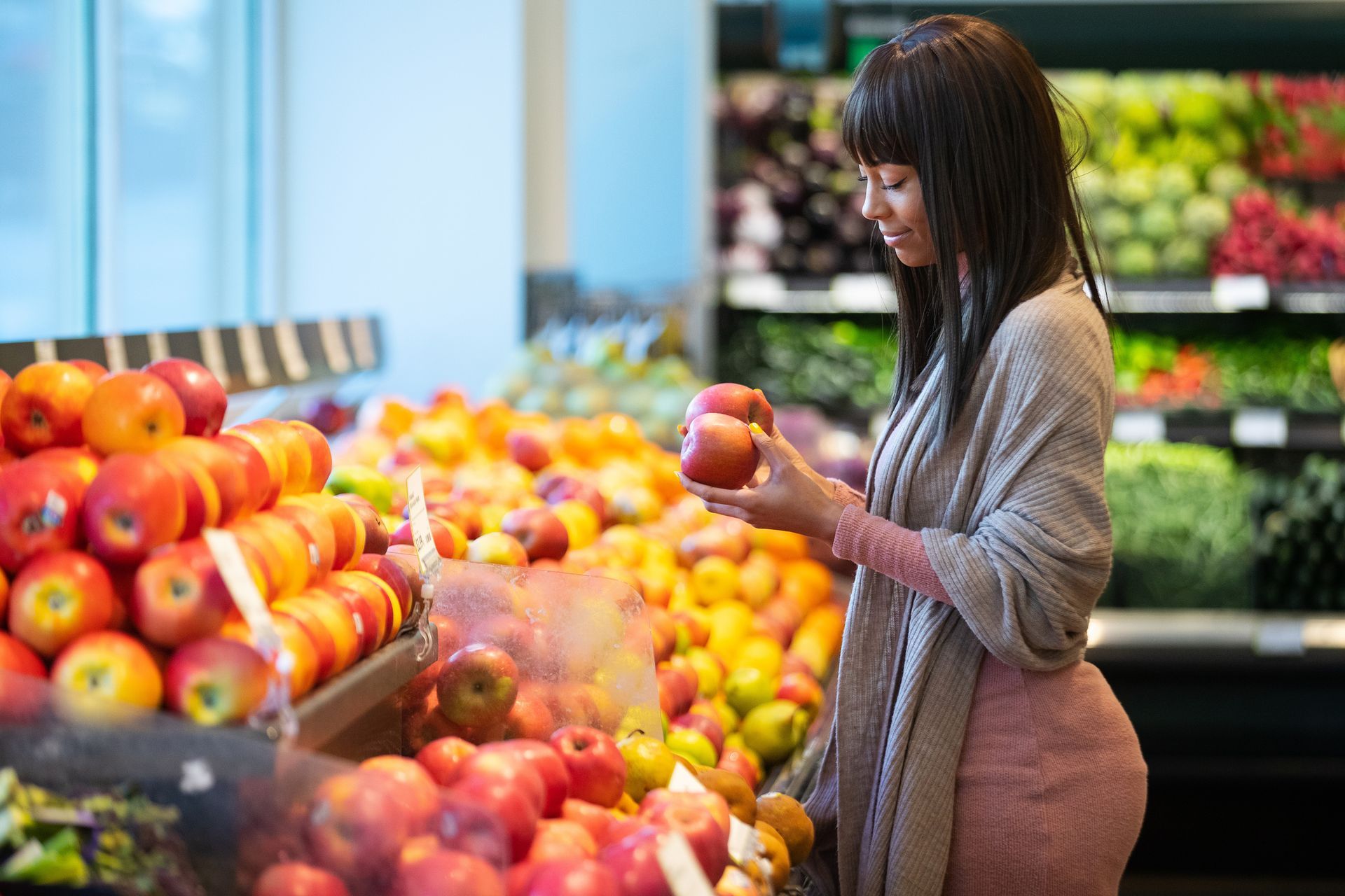 Woman selecting an apple in a grocery produce aisle