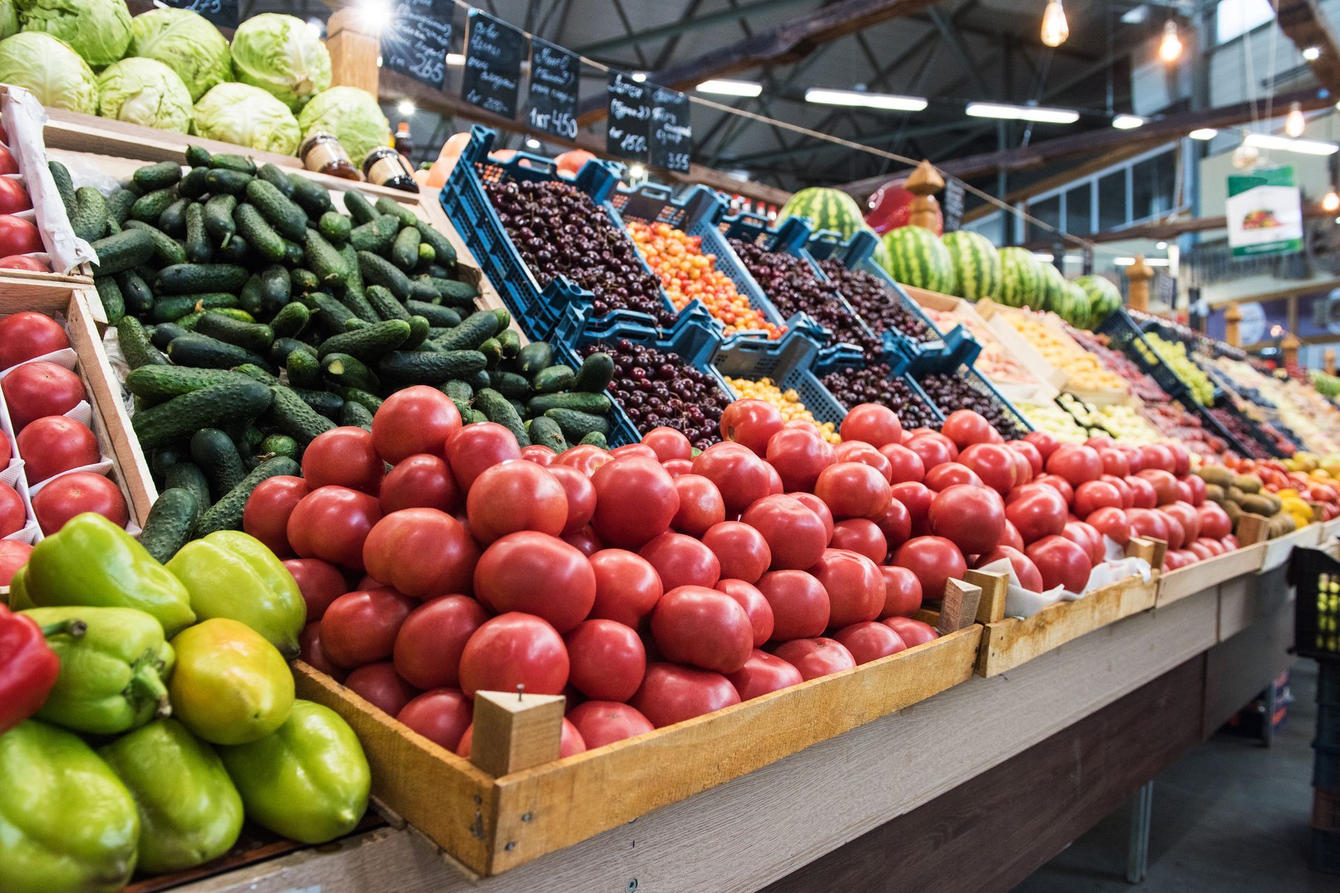 Colorful produce display at a grocery market with tomatoes, cucumbers, peppers, and greens.