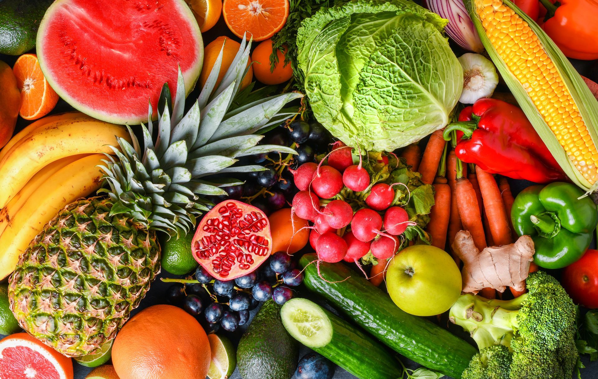 Assorted fresh fruits and vegetables, including pineapple, watermelon, lettuce, peppers, grapes, and cucumbers.