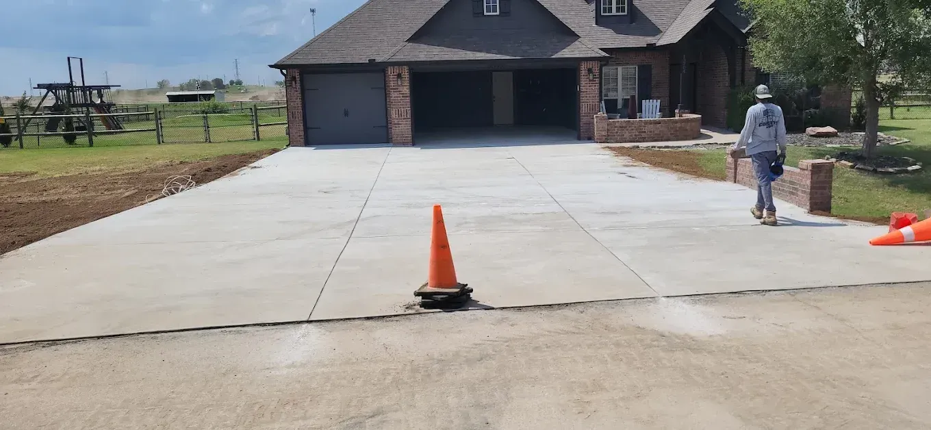 Workers pouring concrete into a form on a sidewalk. One wears orange safety vest.
