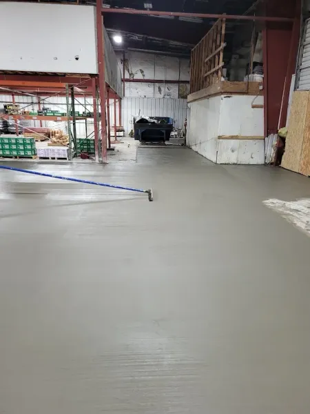 Person in yellow boots using a rake to smooth wet concrete on a construction site.
