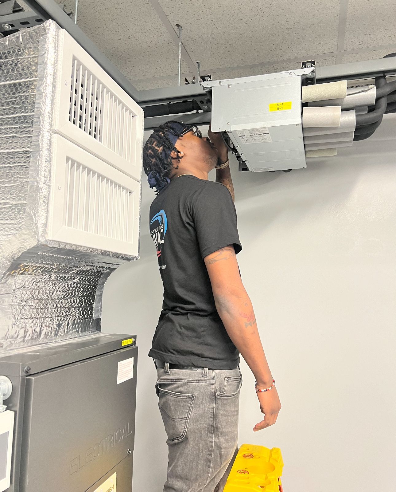 A man is standing on a ladder installing an air conditioner in a living room.