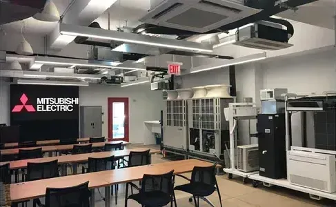 A large room with tables and chairs and a mitsubishi electric sign on the wall.