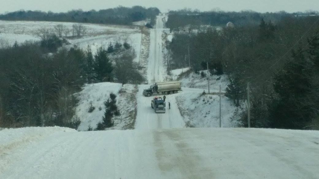 heavy duty wrecker assisting a semi truck at the bottom of a steep snowy road